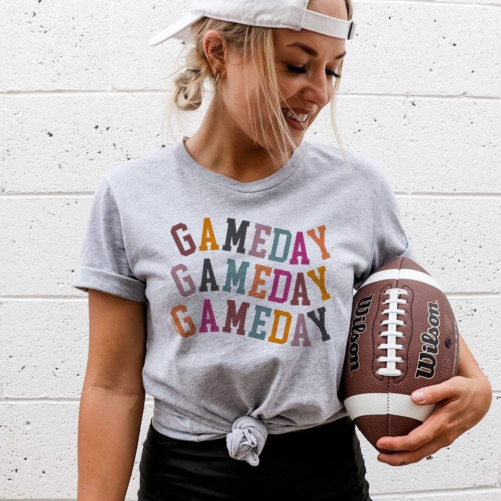 Model is wearing a gray short sleeve crewneck tee featuring a multicolor graphic of the words "Gameday"