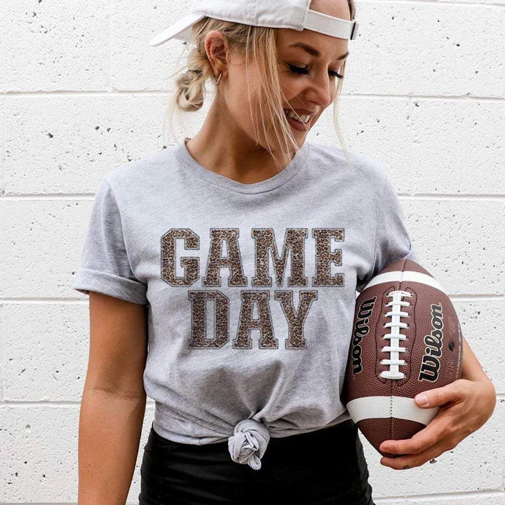Model is wearing a gray short sleeve crewneck tee featuring a leopard print graphic that says "Game day"