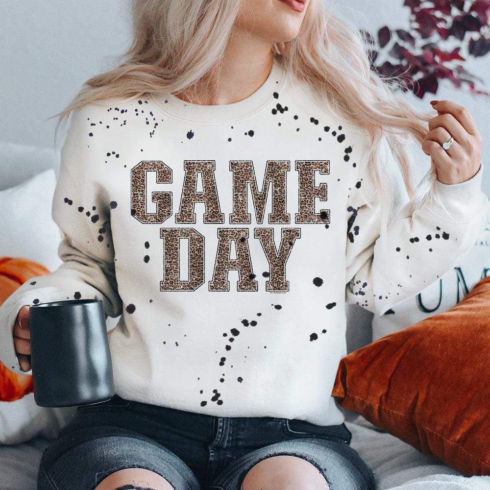 Model is wearing a white sweatshirt featuring a black splatter design and a leopard print graphic that says "Game day"