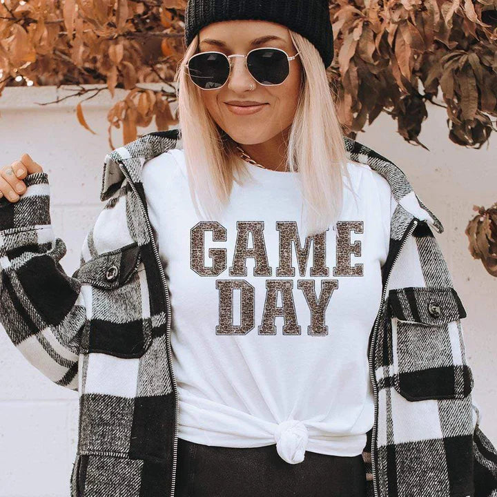 Model is wearing a white short sleeve crewneck tee featuring a leopard print graphic that says "Game day"