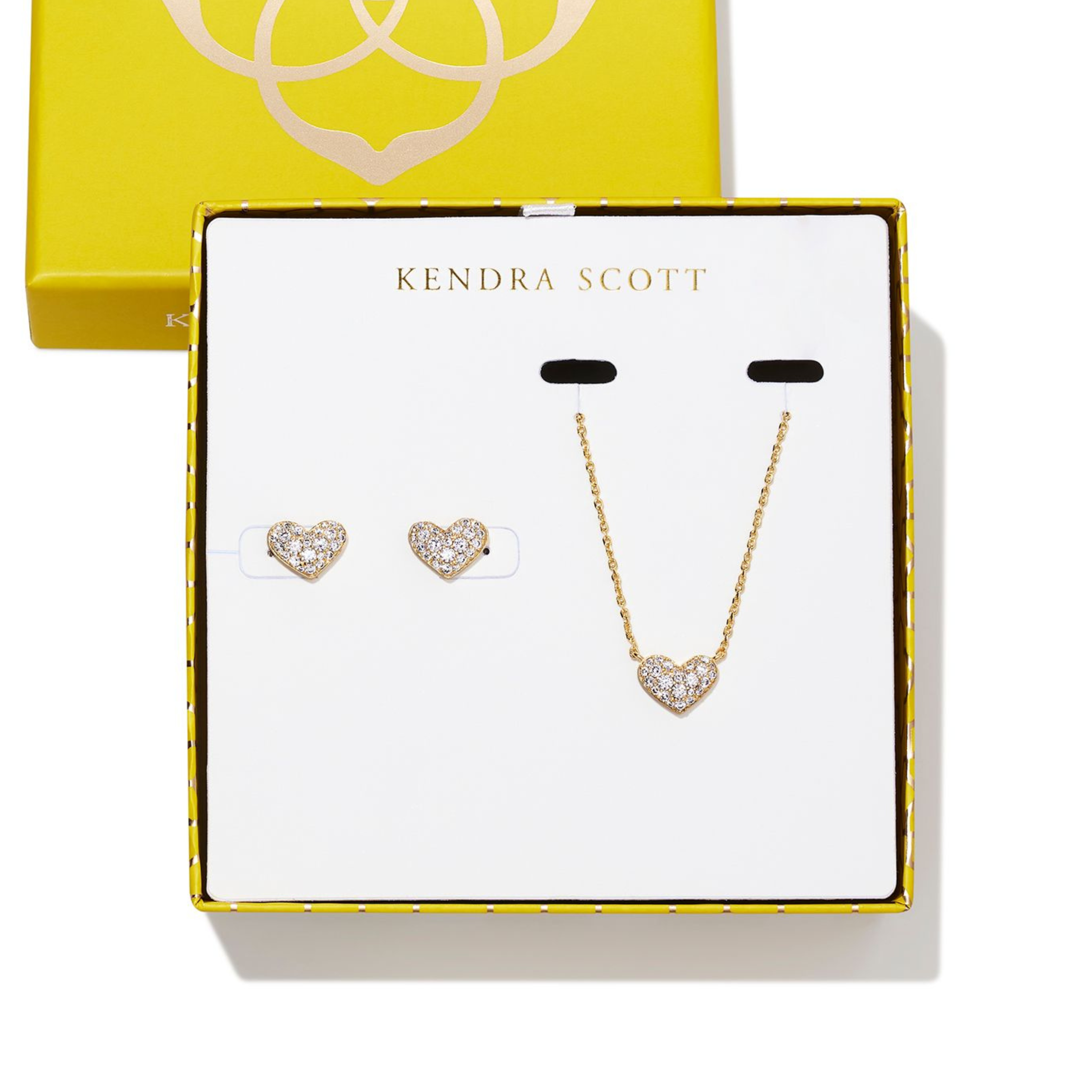 Gold necklace with heart pendnant and gold heart earrings pictured on a Kendra Scott box. The hearts are encrusted with clear crystals.