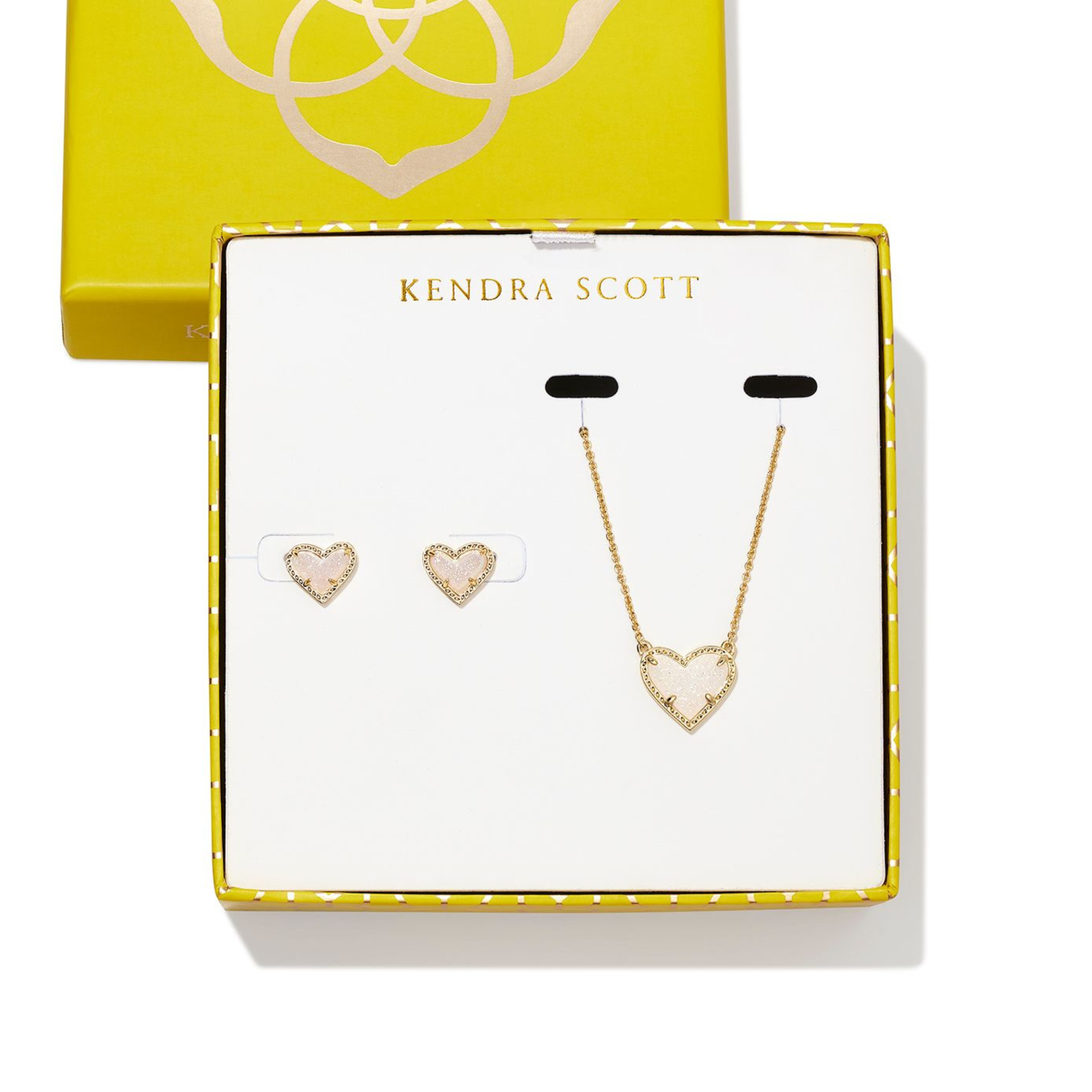 Gold necklace with heart pendnant and gold heart earrings pictured on a Kendra Scott box. The hearts include iridescent drusy stones.