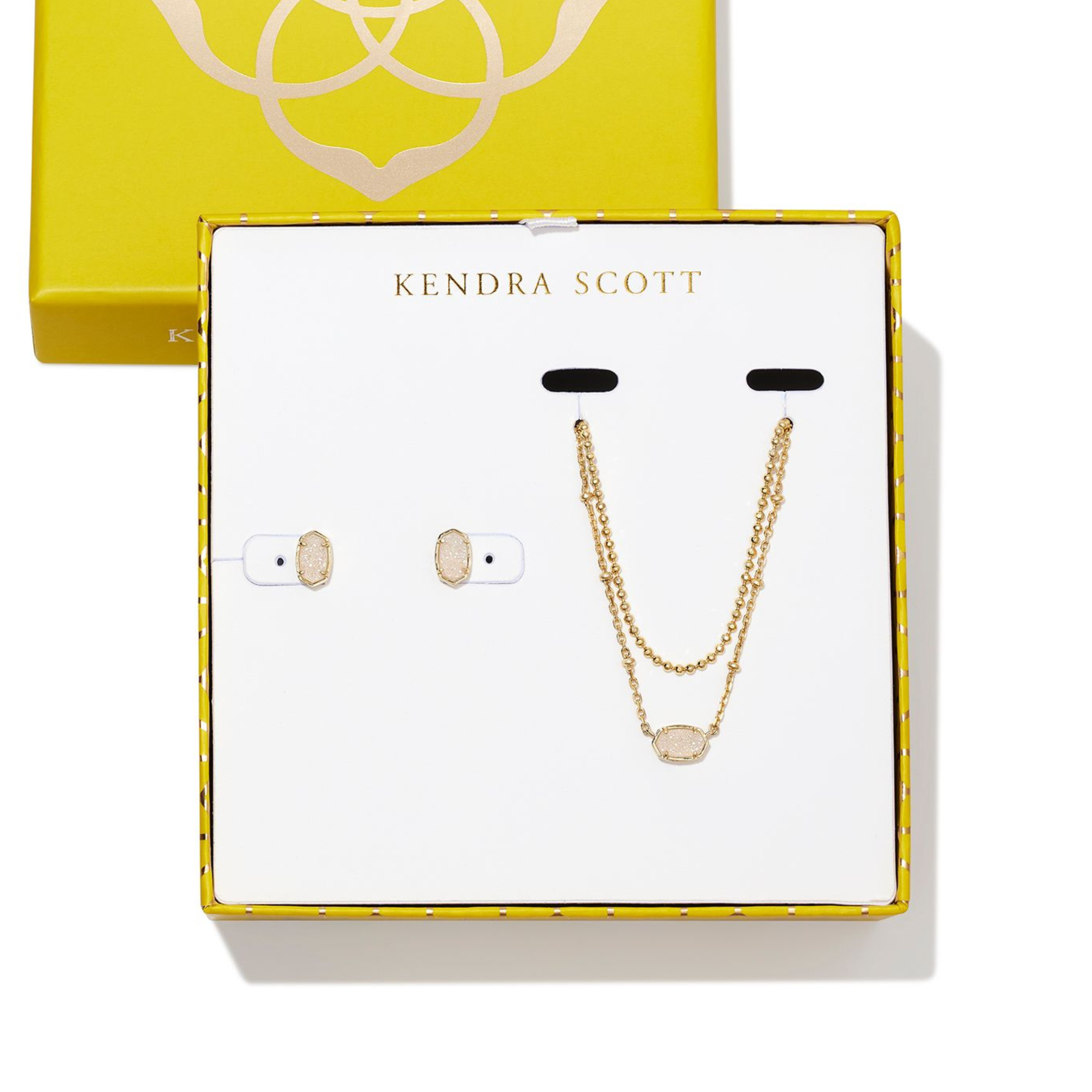 Two gold necklaces with one oval pendnant and gold oval earrings pictured in a Kendra Scott box. The oval pendants include iridescent drusy stones.