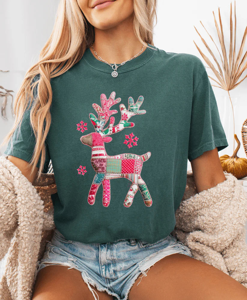 Person wearing a green t-shirt with a colorful reindeer design, sitting in a cozy indoor setting.