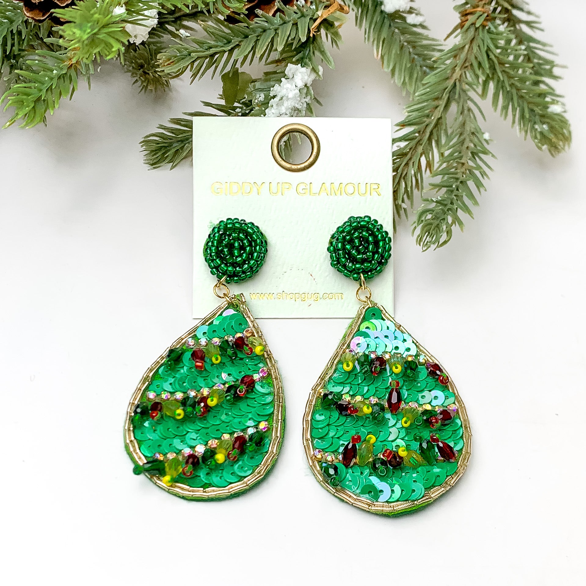 Green sequin beaded teardrop earring with ab crystals and beaded tassels. These earrings are pictured on a white background with pine trees at the top of the picture. 