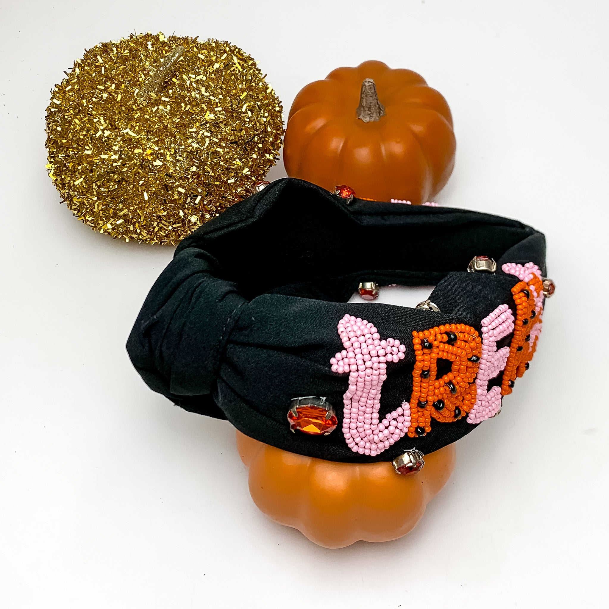 "Trick or Treat" Orange and Pink Beaded Headband in Black. This headband is pictured on a white background with pumpkins around the headband for decoration. 