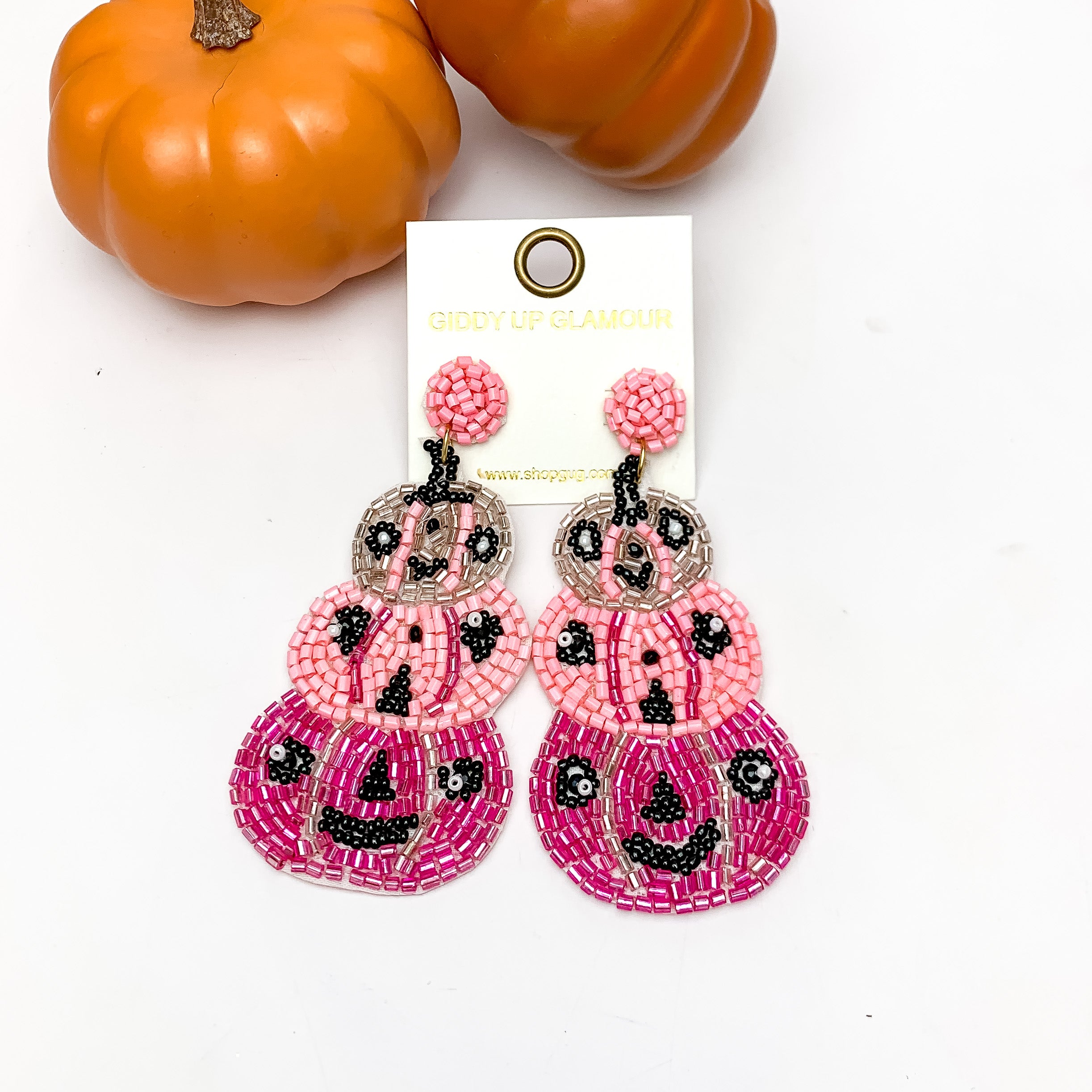 Three Tier Pumpkin Beaded Earrings in Pink. These earrings are pictured on a white background with pumpkins behind the earrings.