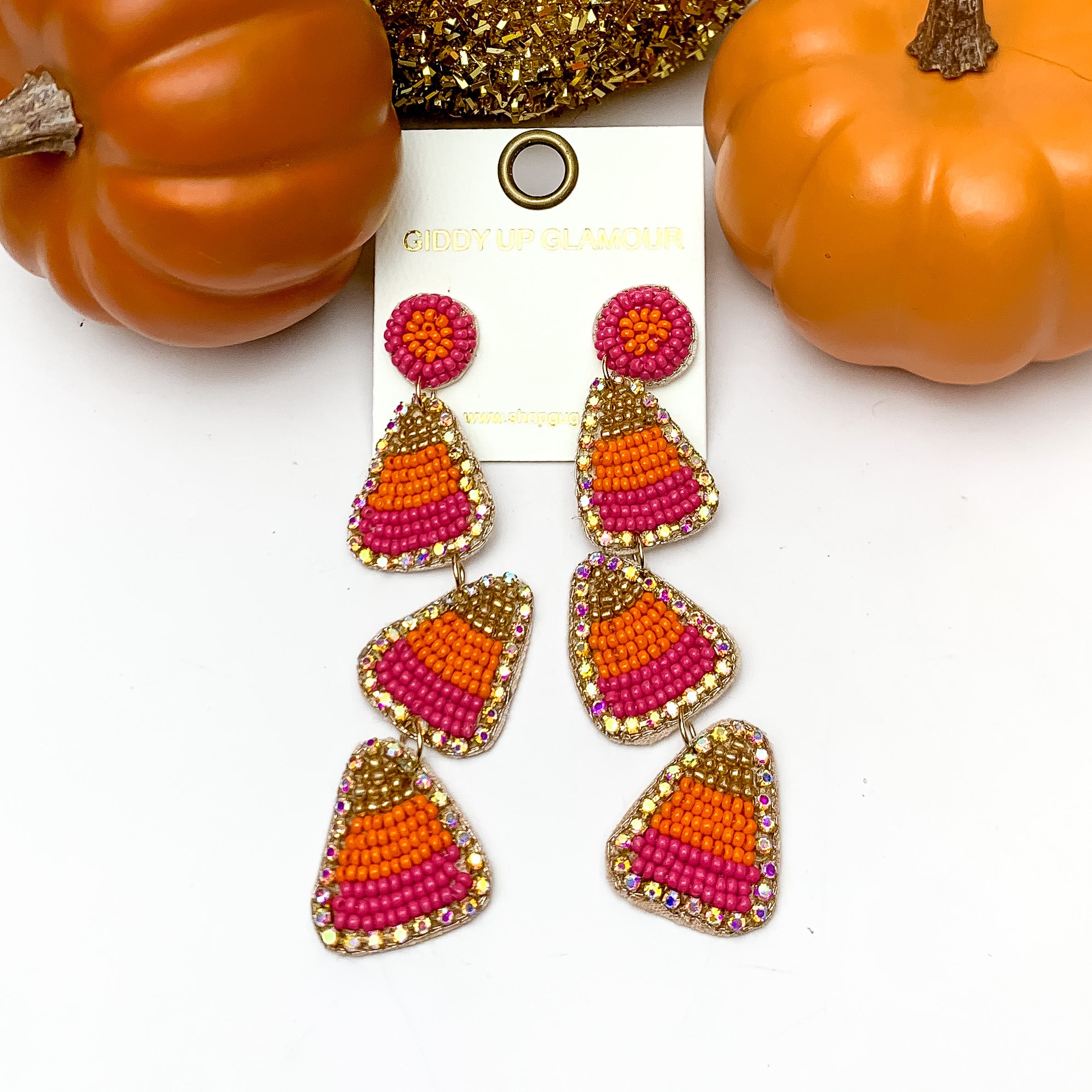 Three Tier Candy Corn Beaded Earrings in Orange and Pink. These earrings are pictured on a white background with pumpkins behind the earrings.