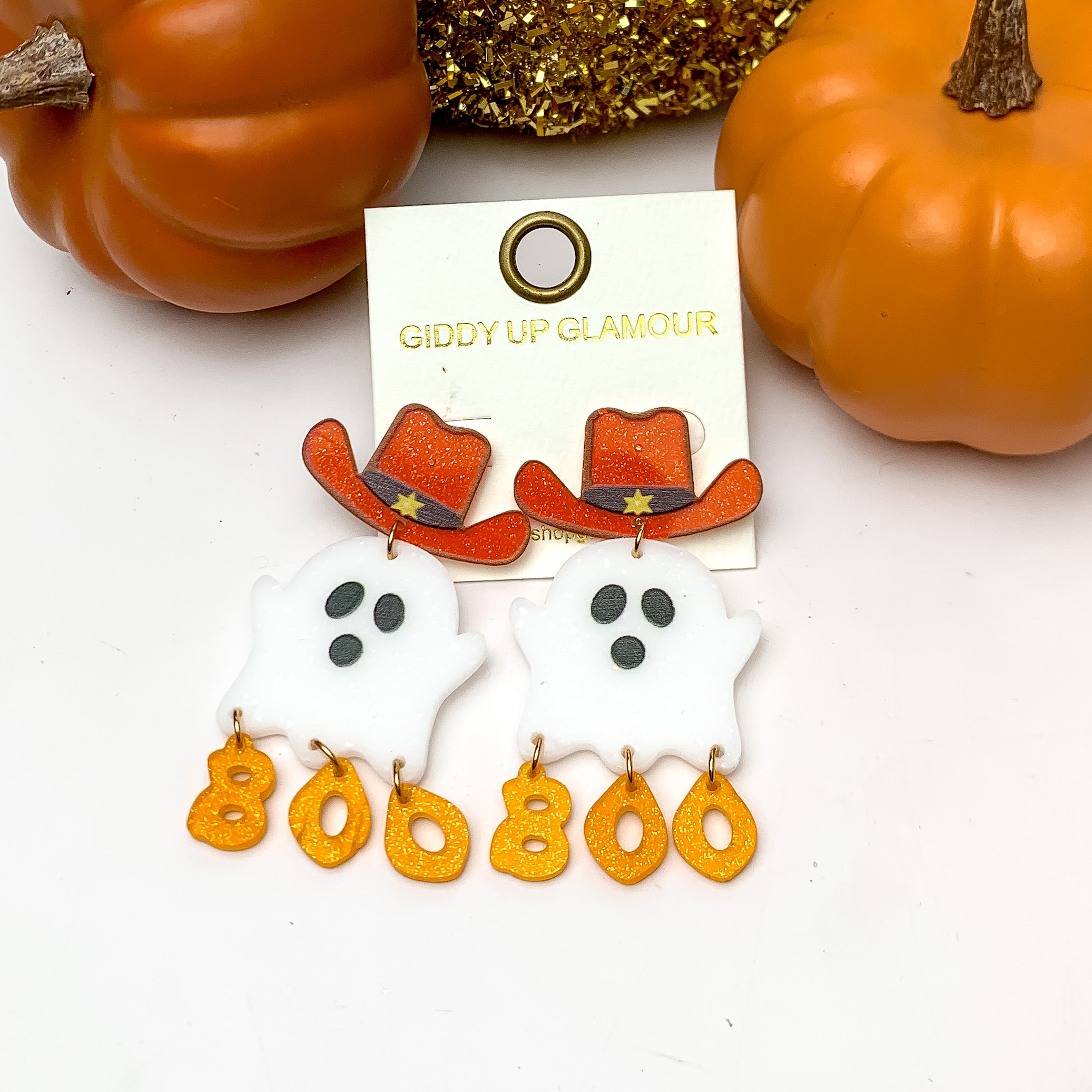 Halloween Ghost Earrings With Dangling Boo Letters. These earrings are pictured on a white background with pumpkins behind the earrings.