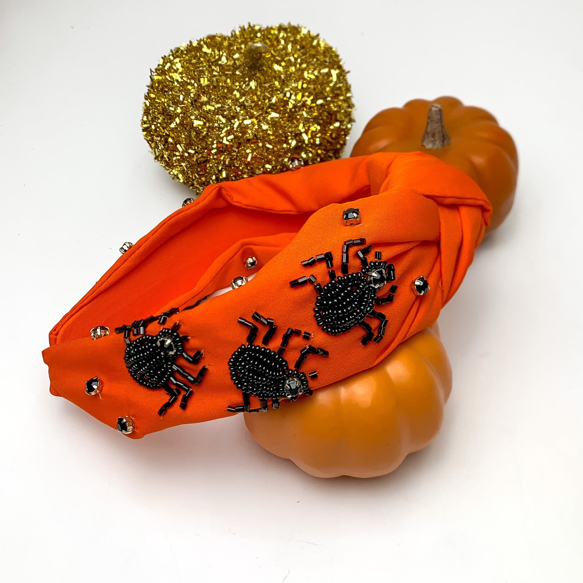 Halloween Orange Headband With Black Spiders. This headband is pictured next to decorative pumpkins.
