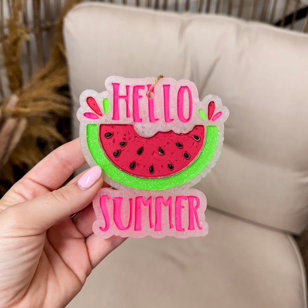wooden rustic background with a car freshie that looks like a watermelon and the words "hello summer"