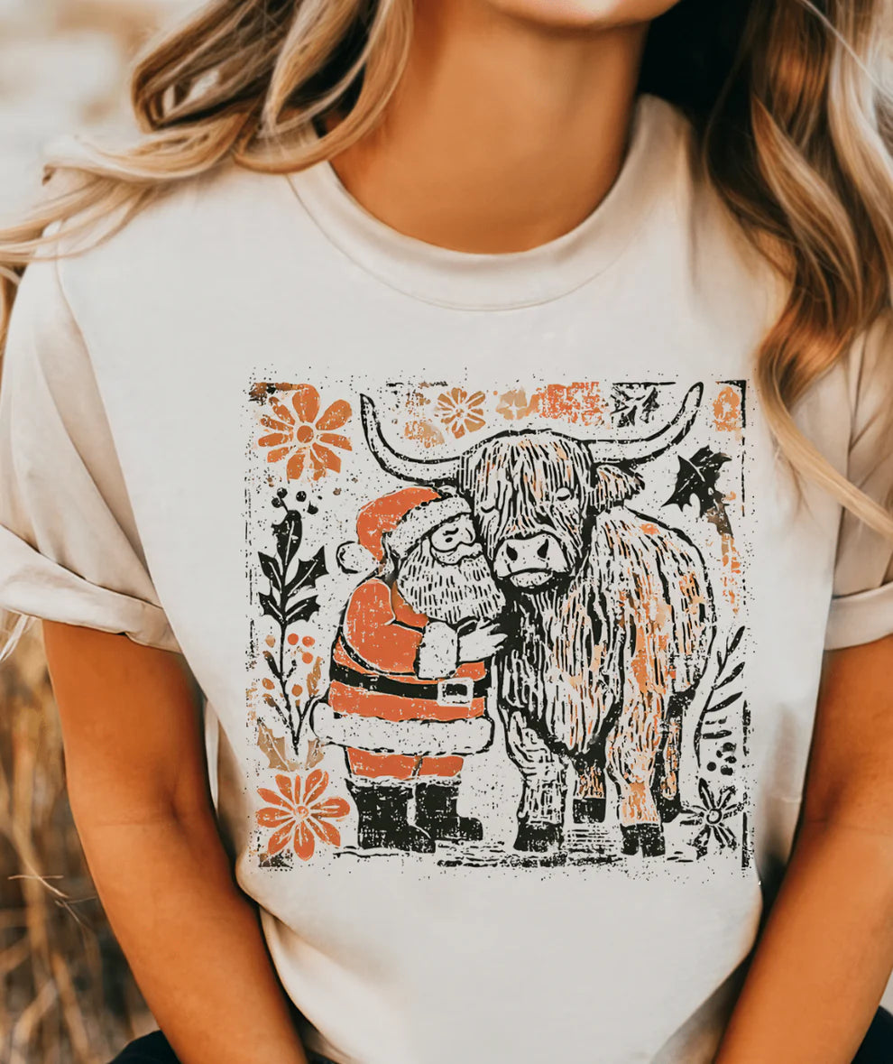 Woman wearing cream t-shirt with Highland cow and Santa graphic, rustic Christmas design