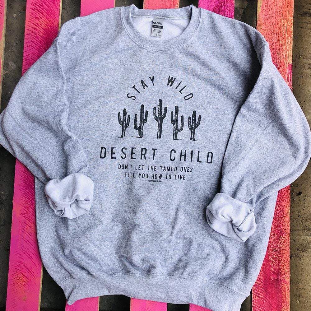 A heather grey crewneck sweatshirt with 5 cacti in the center of the sweatshirt. The words "stay wild" can be found above the cacti and "desert child. Dont let the tamed ones tell you how to live" can be found below the cacti