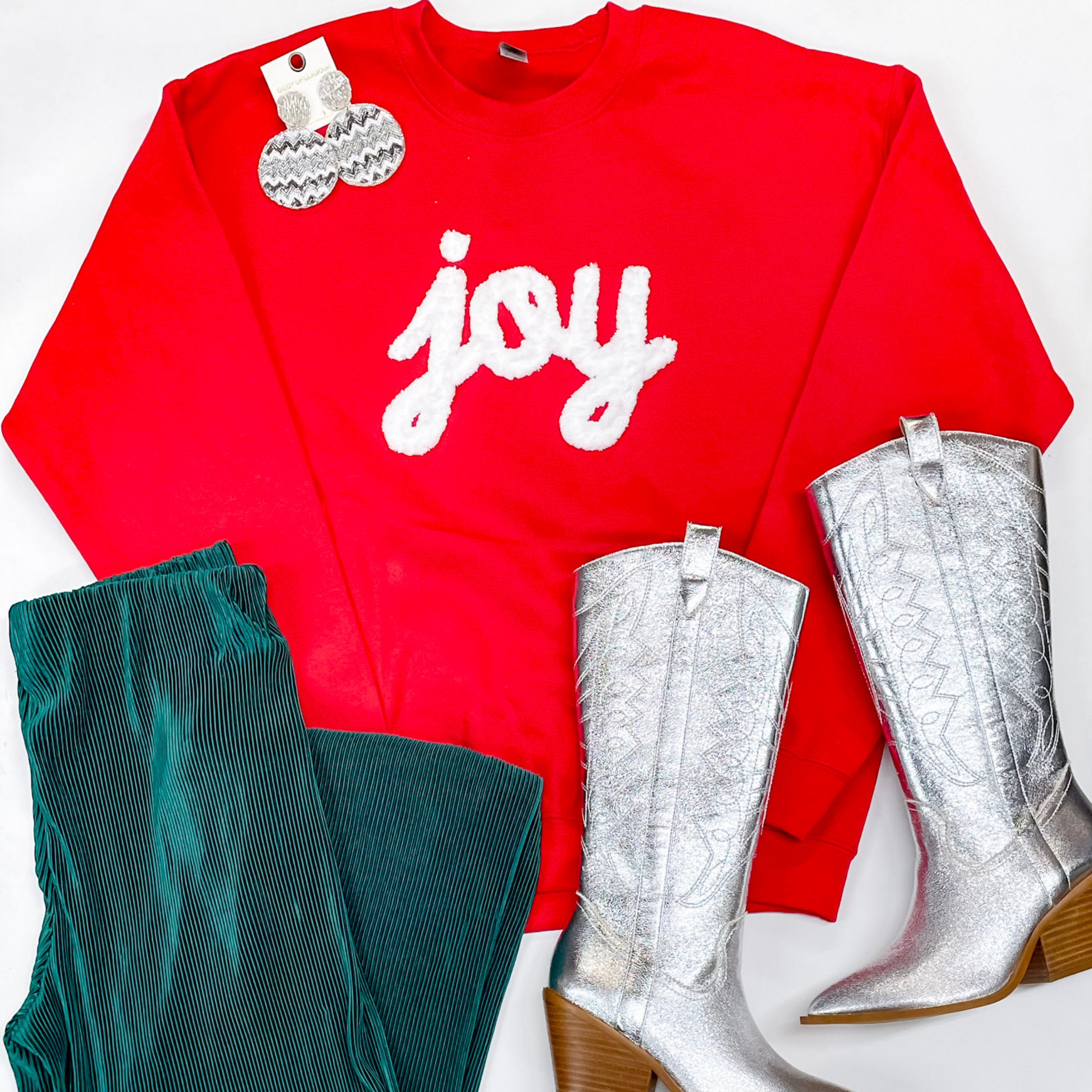 Photo feature a red hand stitched sweatshirt with the word "joy" on the front. That is paired with green pants, silver Dingo boots, and silver jewelry. 