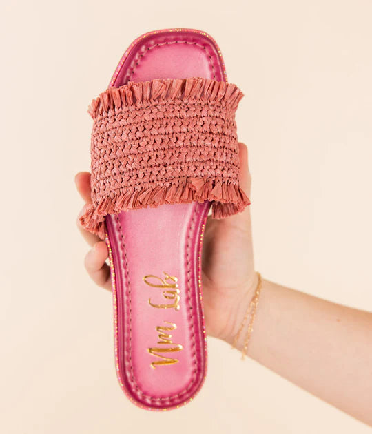 Pink woven sandal held by a hand against a beige background