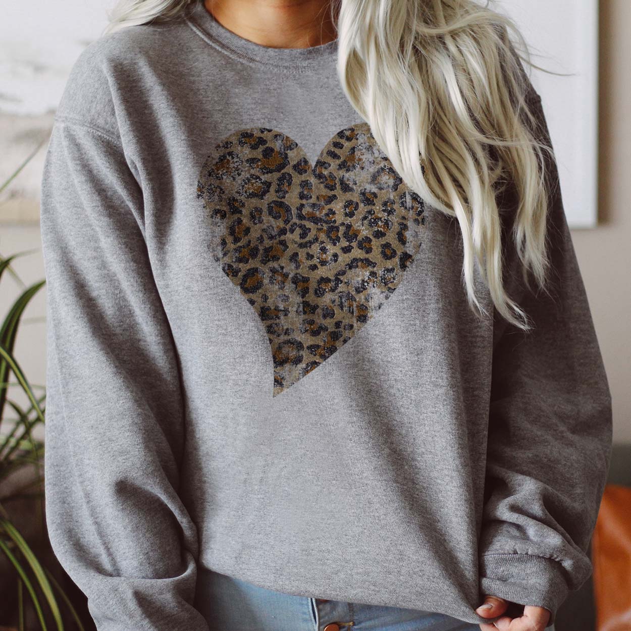 Model is wearing a grey long sleeve sweatshirt with a washed leopard heart graphic. 