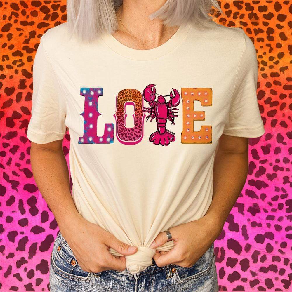 A short sleeve cream tee with the word "love" in the center. The L is purple and blue with white dots through the center, the O is an orange to pink ombre cheetah print, the V is a pink lobster, and the E is orange with rhinestones in the middle. 