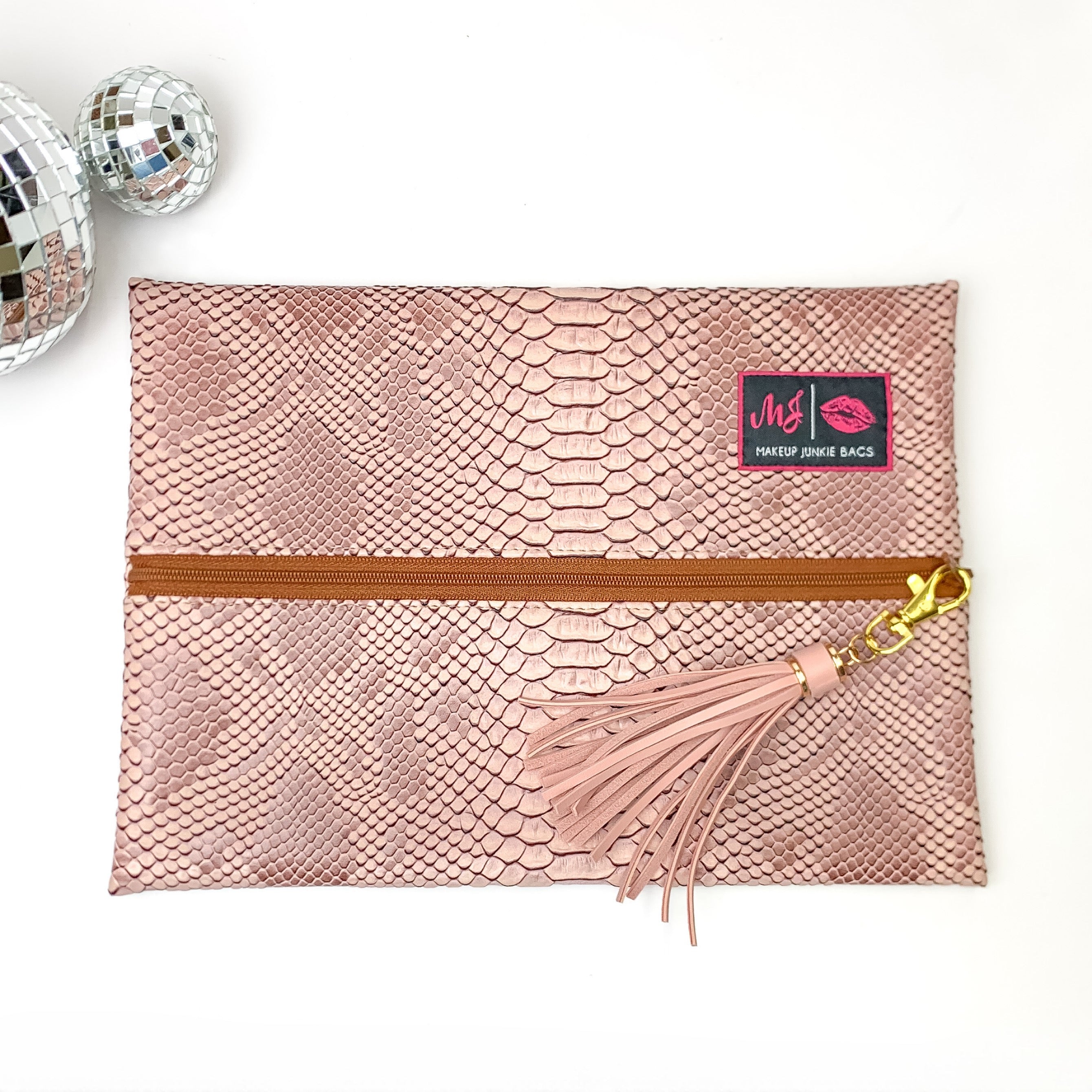 Pictured on a white background with disco balls at top is a lay flat bag in a copper snake print. This bag includes a middle zipper and a tassel.