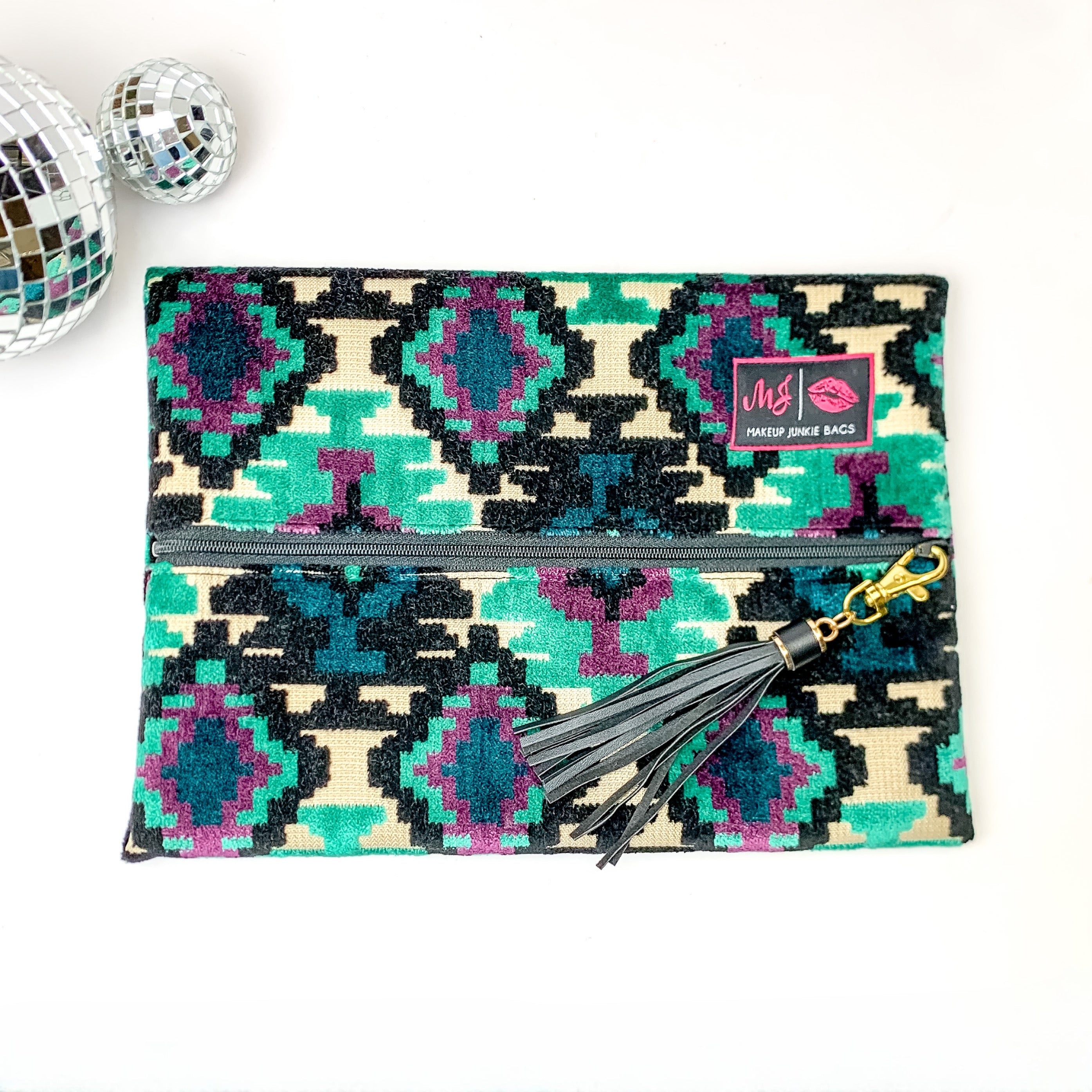 Pictured on a white background with disco balls at top is a lay flat bag in a midnight aztec print. This bag includes a middle zipper and a tassel.