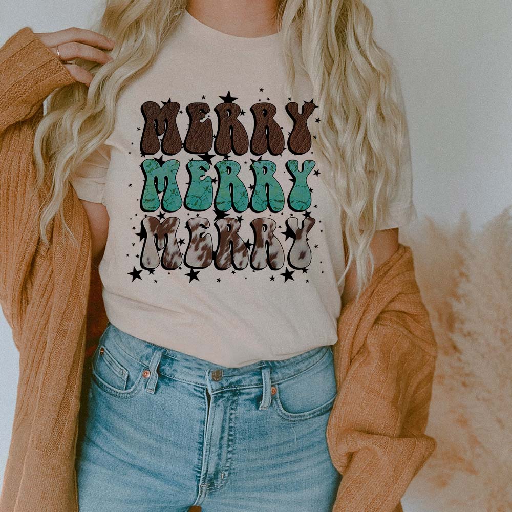 This cream tee includes a crew neckline, short sleeves, and a cute Christmas graphic of the words "MERRY MERRY MERRY". The words are in cowhide and turquoise and stacked on each other with black stars all over. This tee is being modeled with rolled sleeves, a camel cardigan, and a pair of light wash denim jeans. 
