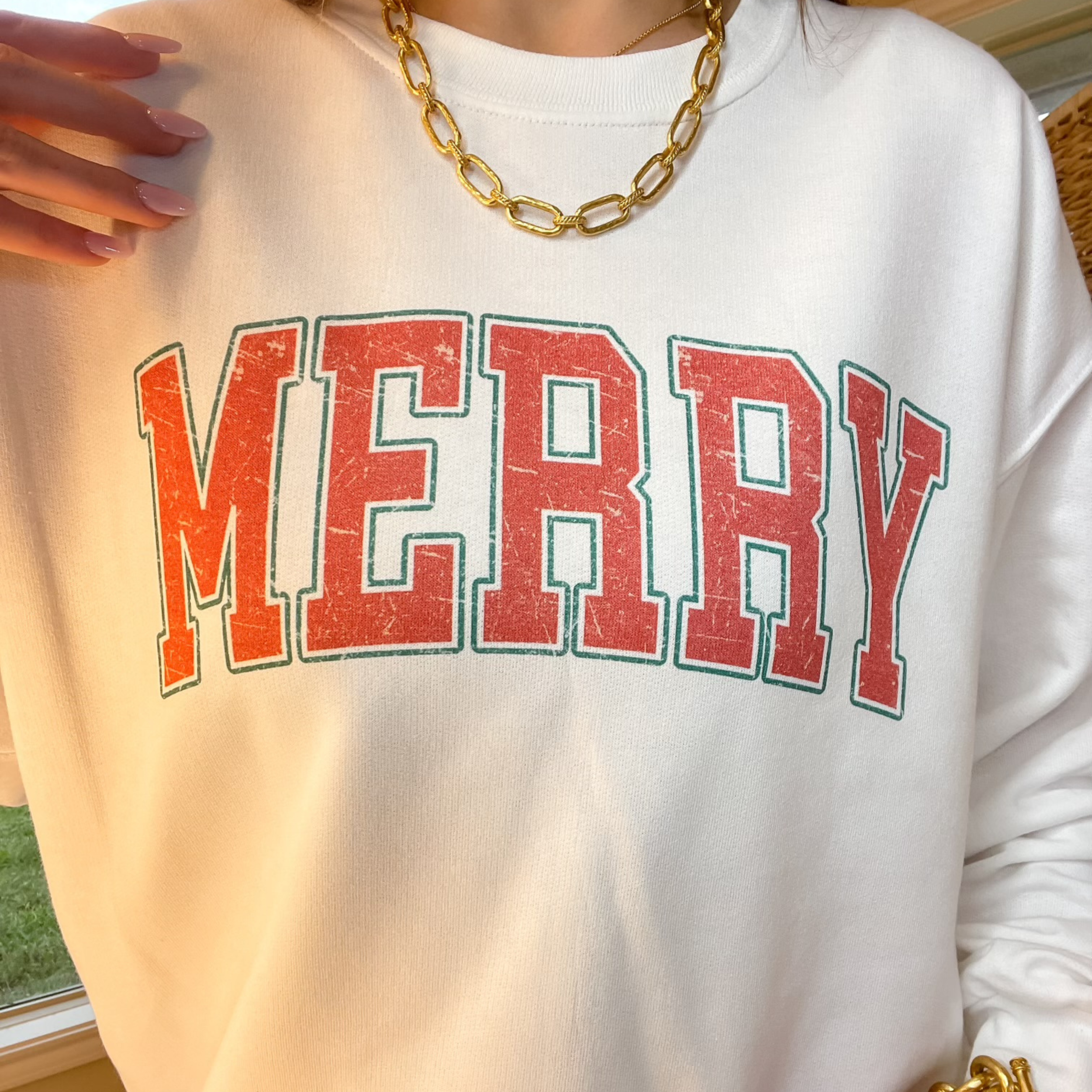 Photo features a cream sweatshirt with the word "MERRY" across the front in red with an outline of green. 