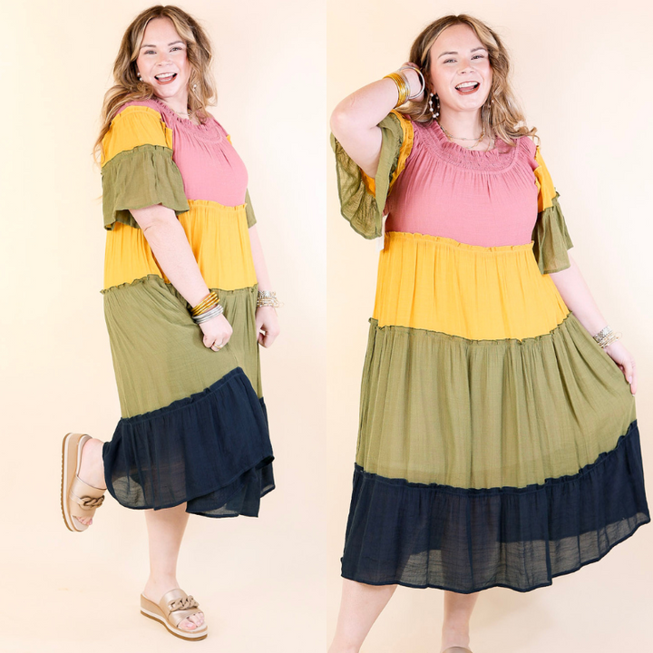 Model is wearing a color block midi dress in mustard, olive, mauve, and navy. The dress features ruffle tiers.