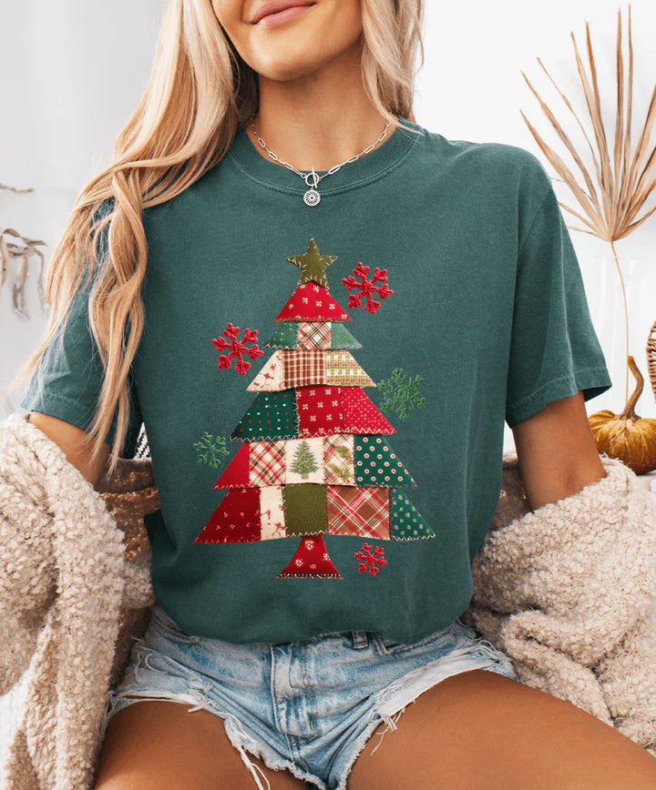Person wearing a green t-shirt with a Christmas tree design, sitting indoors.