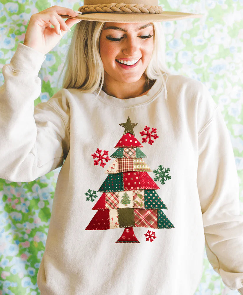 Woman wearing a white sweatshirt with a Christmas tree design, holding a straw hat against a floral background.