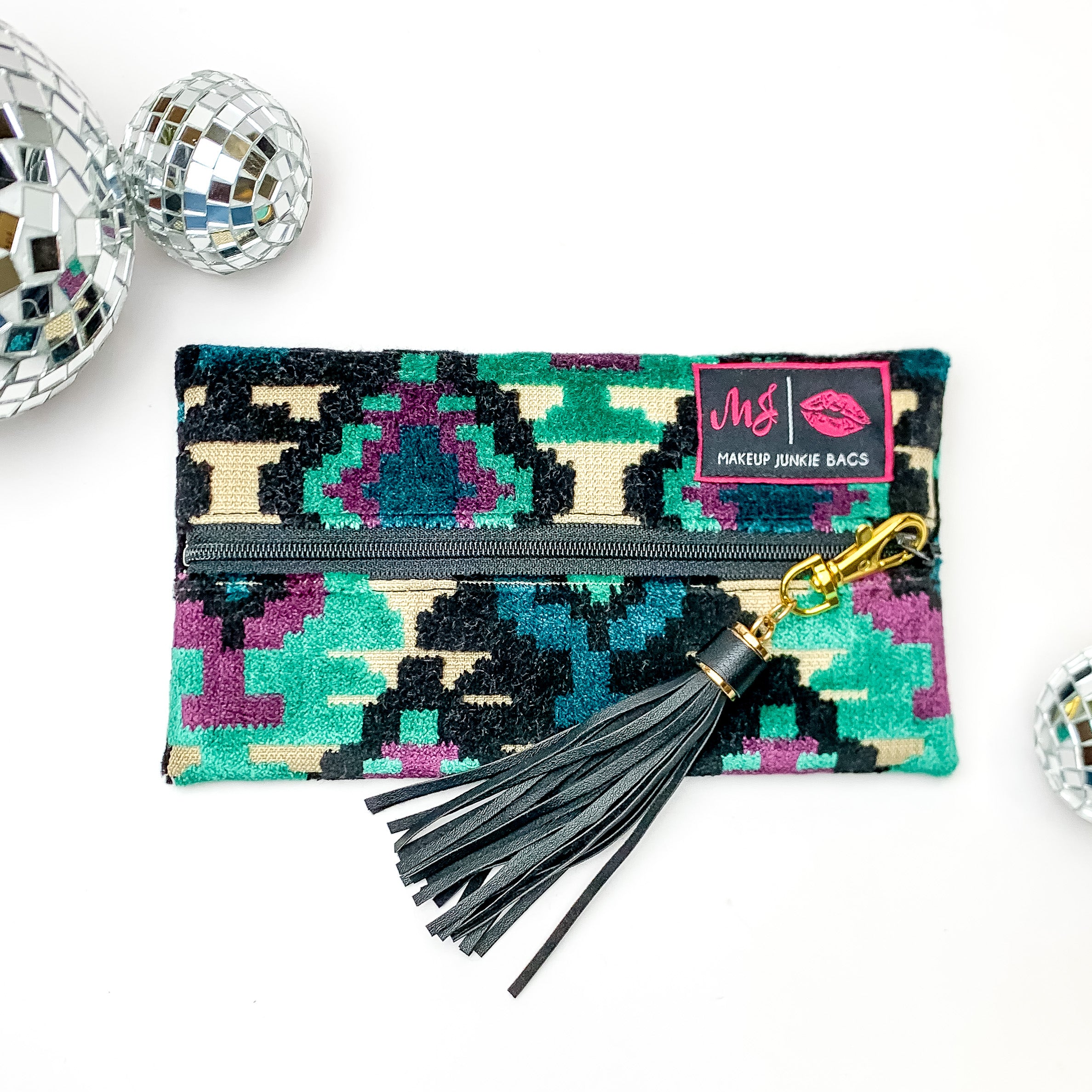 Pictured on a white background with disco balls at top is a mini lay flat bag in a midnight aztec print. This bag includes a middle zipper and a tassel. 