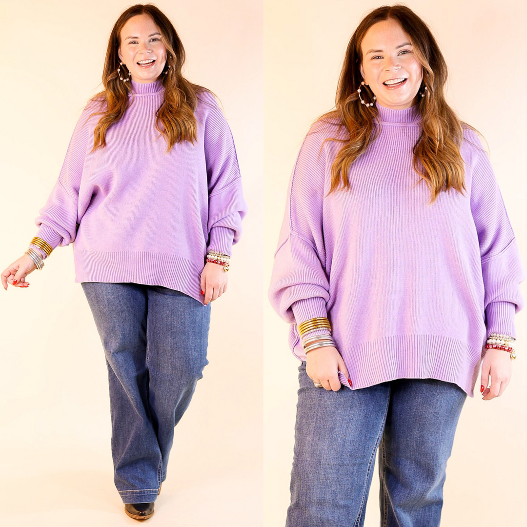 Model is wearing lavender purple oversized sweater with side slit with jeans. Against a plain background. 