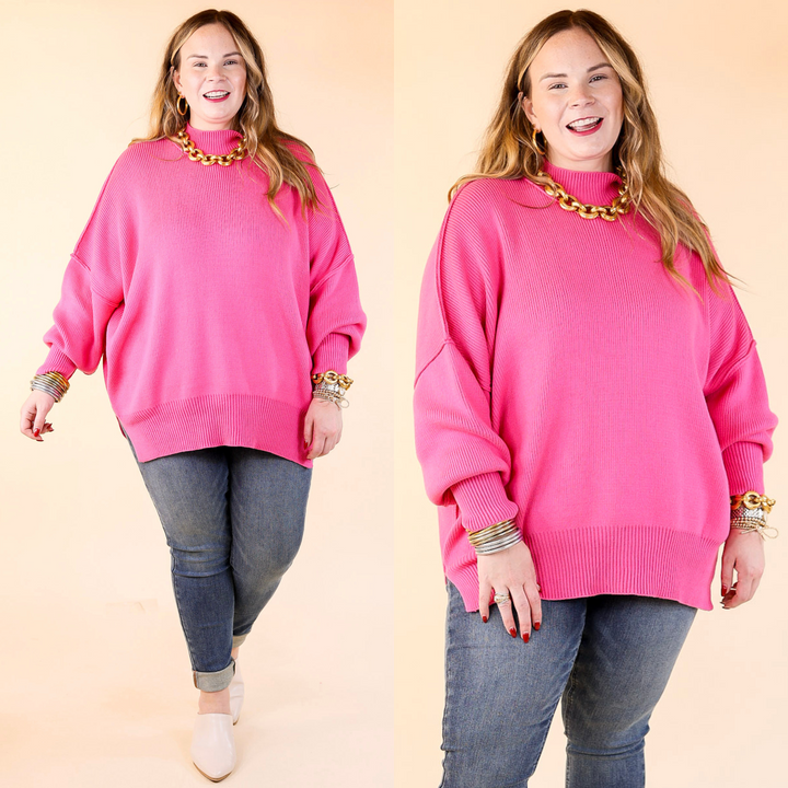 Model is wearing pink oversized sweater with side slit with jeans and jewelry. Against a plain background. 