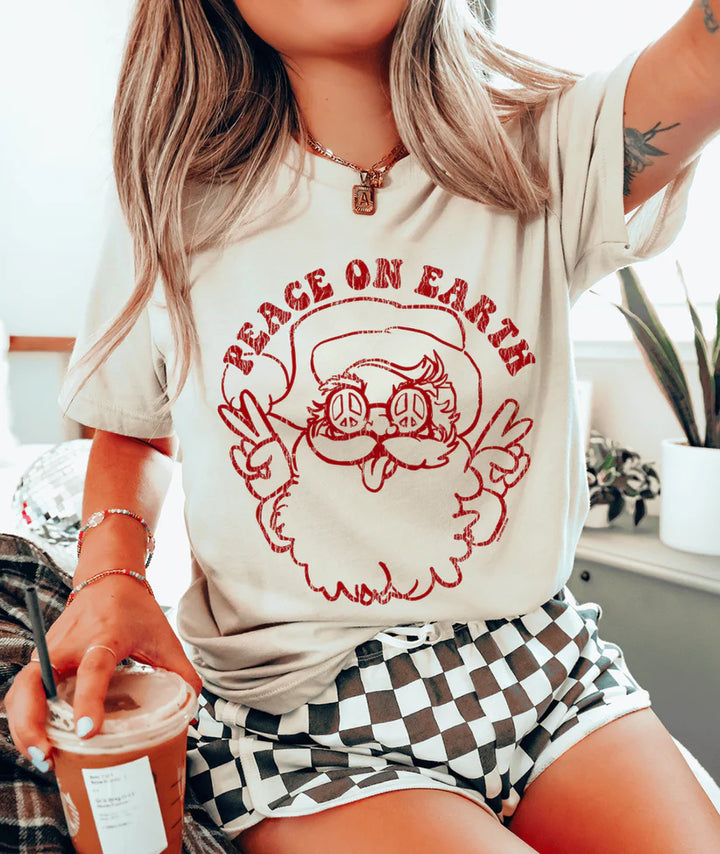 Cream tee with red “Peace on Earth” Santa graphic featuring peace sign sunglasses and retro lettering.