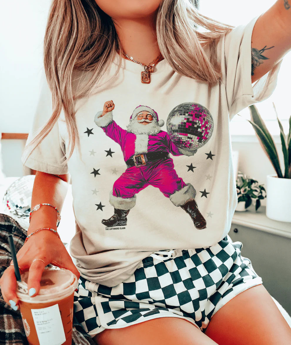 Person wearing a t-shirt with a festive design of a dancing Santa Claus, holding a drink.