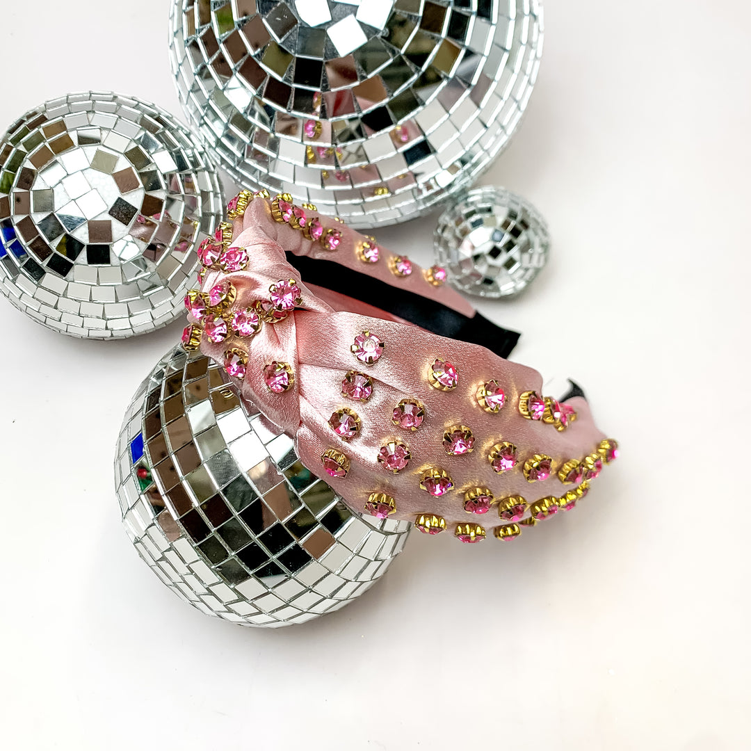 Crystal Detailed Satin Knot Headband in Light Pink. This headband is pictured on a white background and is surrounded by disco balls.
