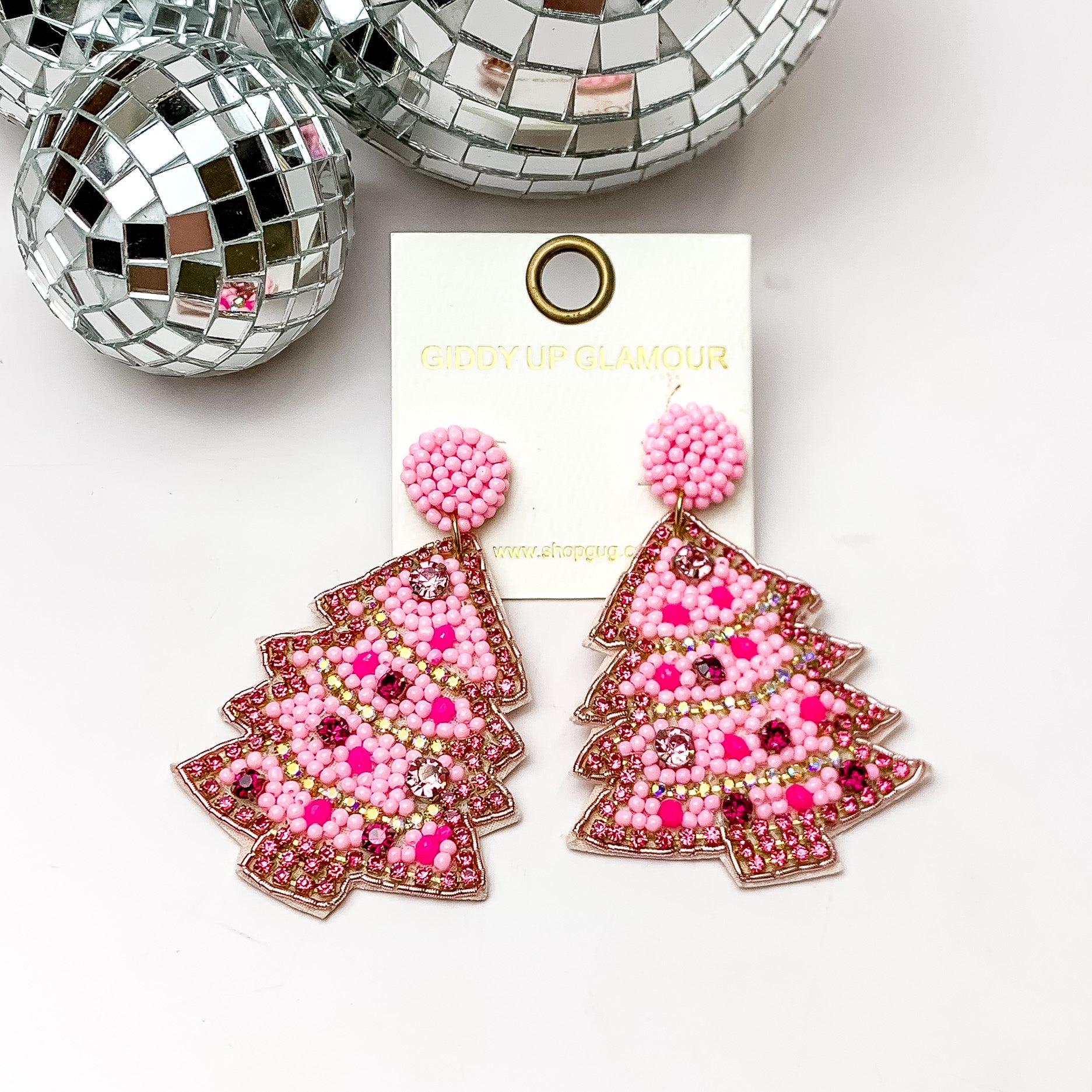 Pink mix beaded Christmas tree earrings with a pink crystal outline. These earrings are pictured on a white background with disco balls at the top. 