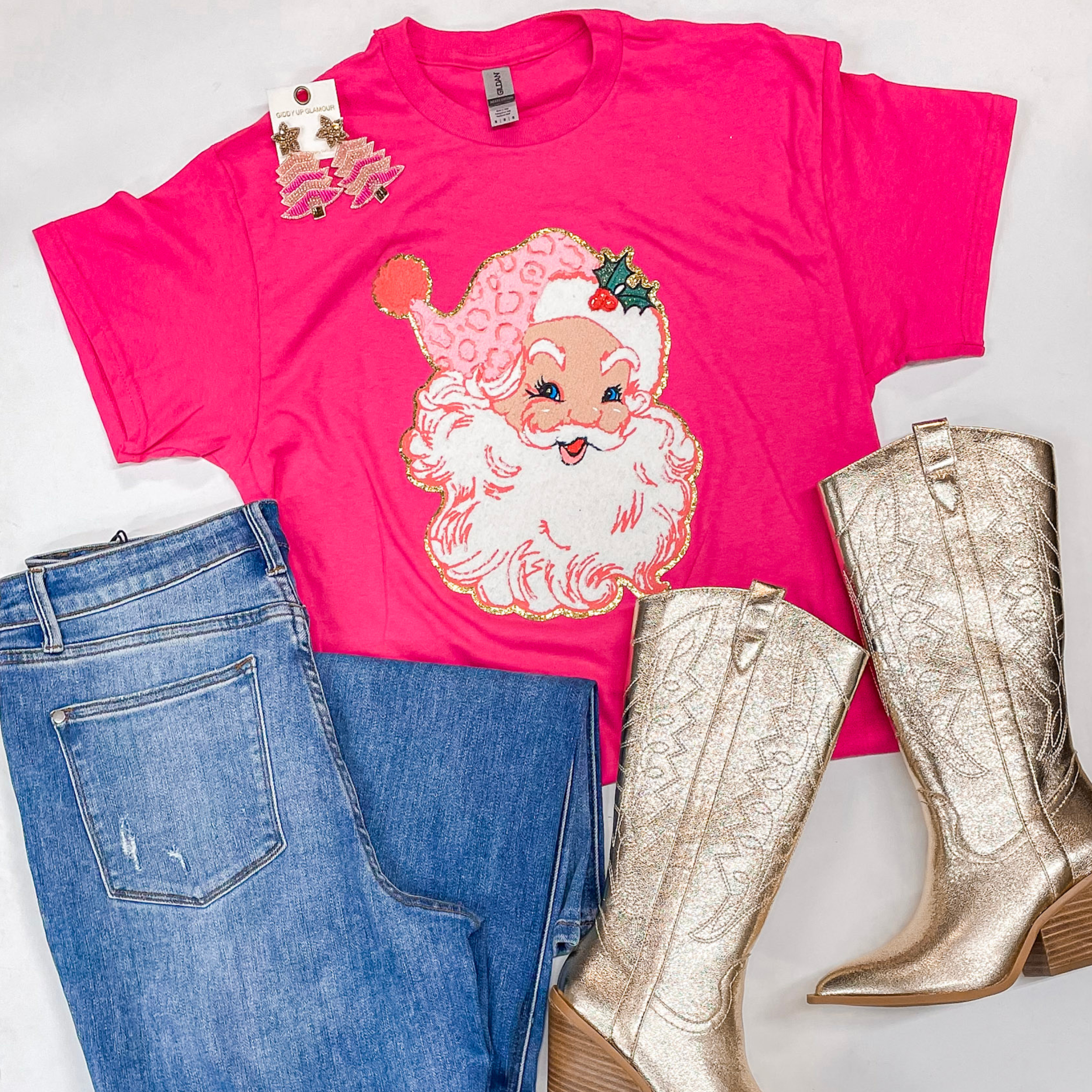 Photo features a dark pink short sleeve tee with a santa patch. This is paired with Judy Blue jeans, gold boots, and pink and gold earrings all on a white background. 