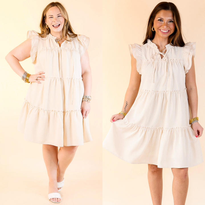 It includes ruffle cap sleeves, a keyhole and tie neckline, a tiered body, and a beige and white pin stripe pattern. Available in sizes small through plus size.