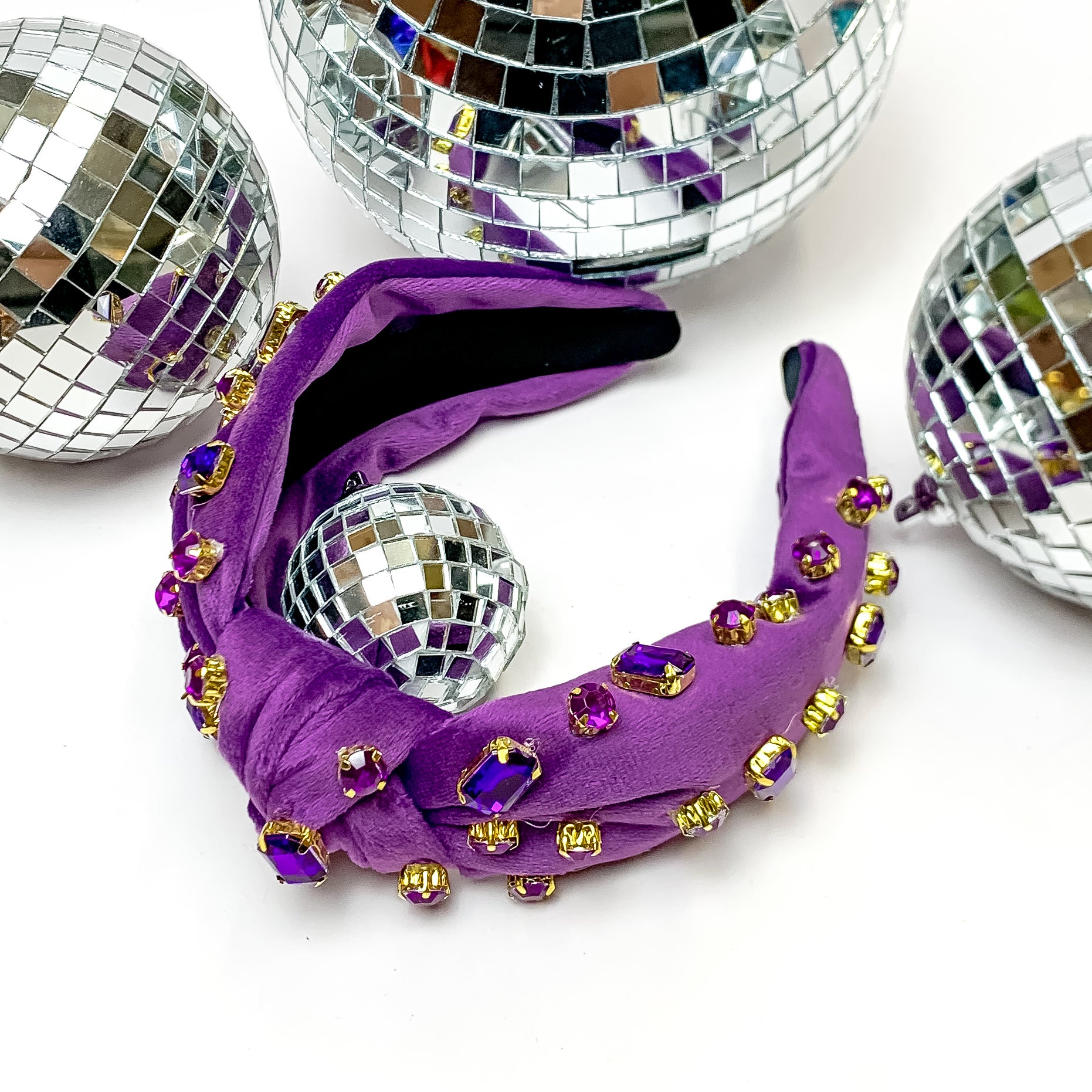 Crystal Detailed Velvet Knot Headband in Purple. This headband is pictured on a white background and is surrounded by disco balls.