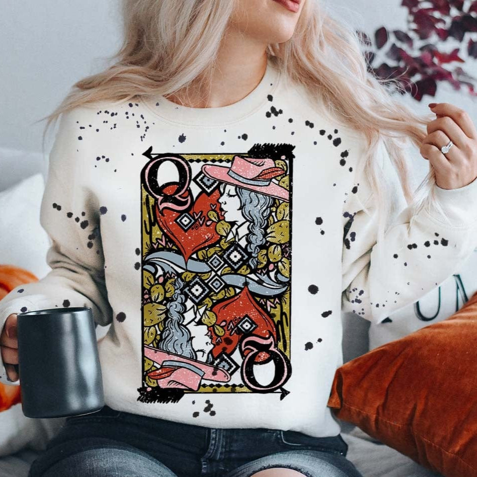 Model is wearing a white long sleeve sweatshirt that has a queen of hearts playing card on the front. The sweatshirt has black splatter paint detailing.