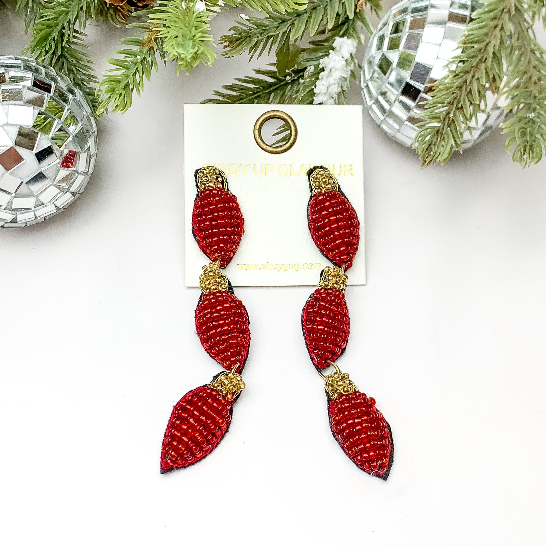 Red beaded Christmas light drop earrings. These earrings are pictured on a white background with pine trees at the top of the picture. 