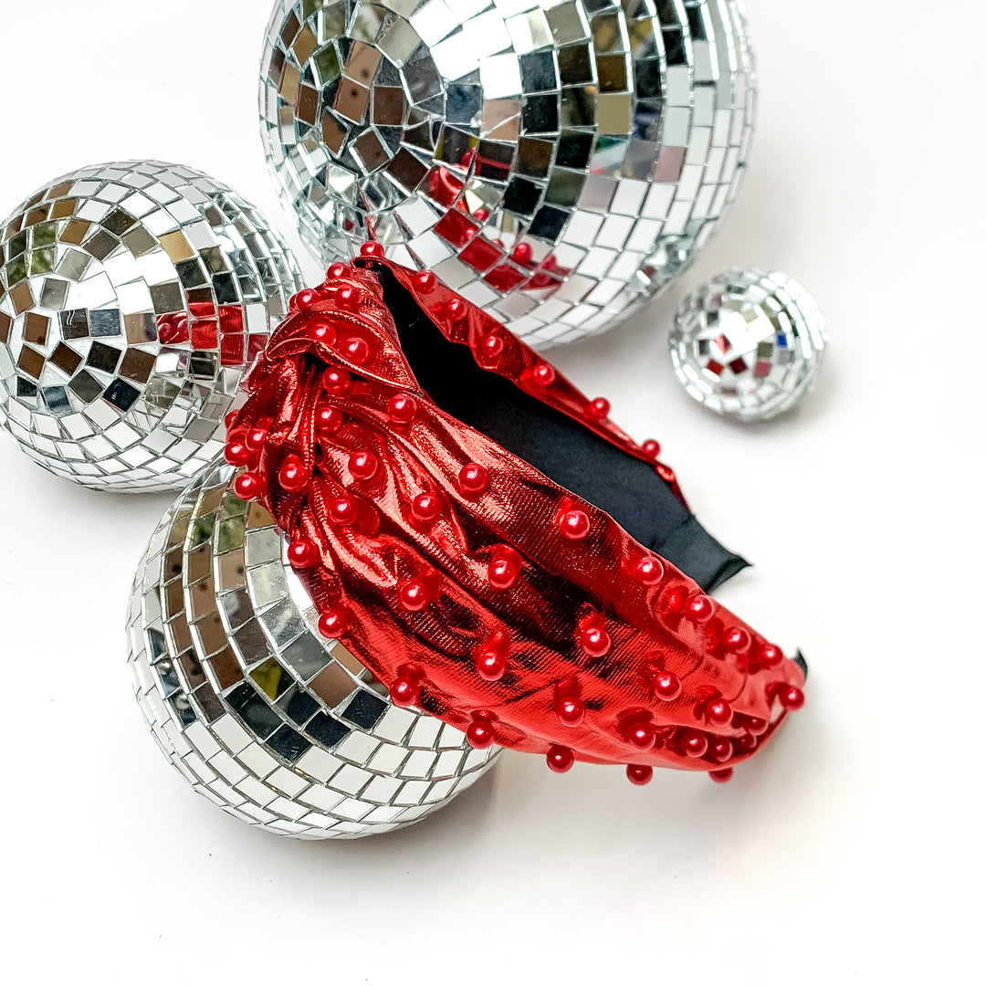 Top of the Charts Red Headband With Red Pearls. This headband is pictured on a white background and is surrounded by disco balls.