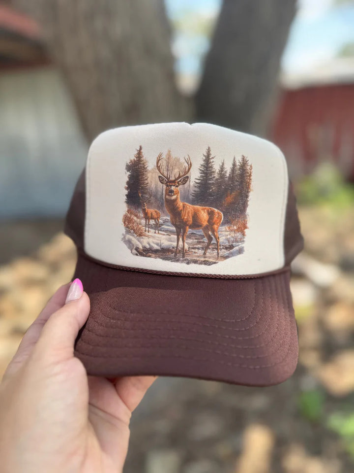 Trucker hat with deer design held by a hand against a blurred natural background