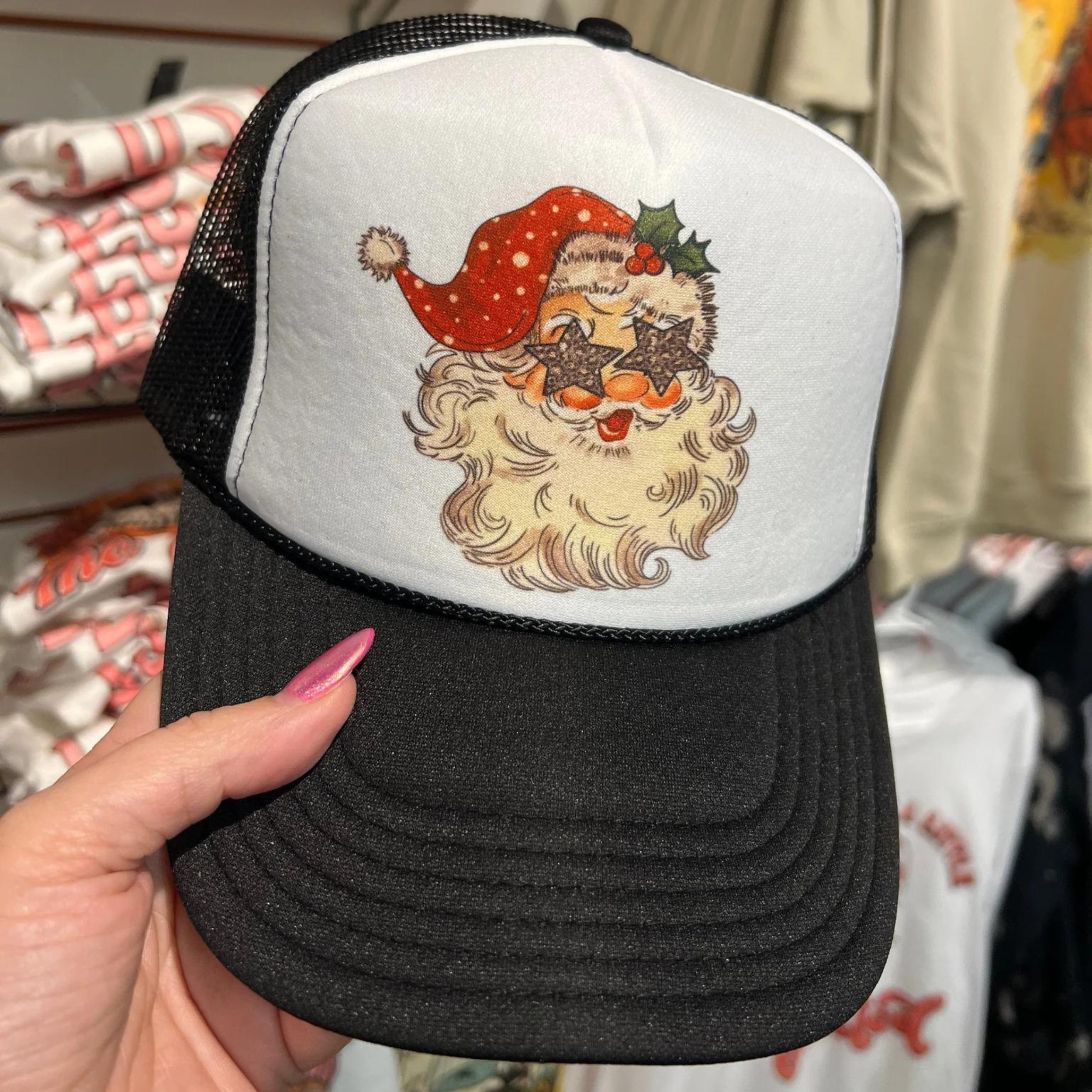 Photo features a black and white trucker hat with Santa's face on the front with star eyes.