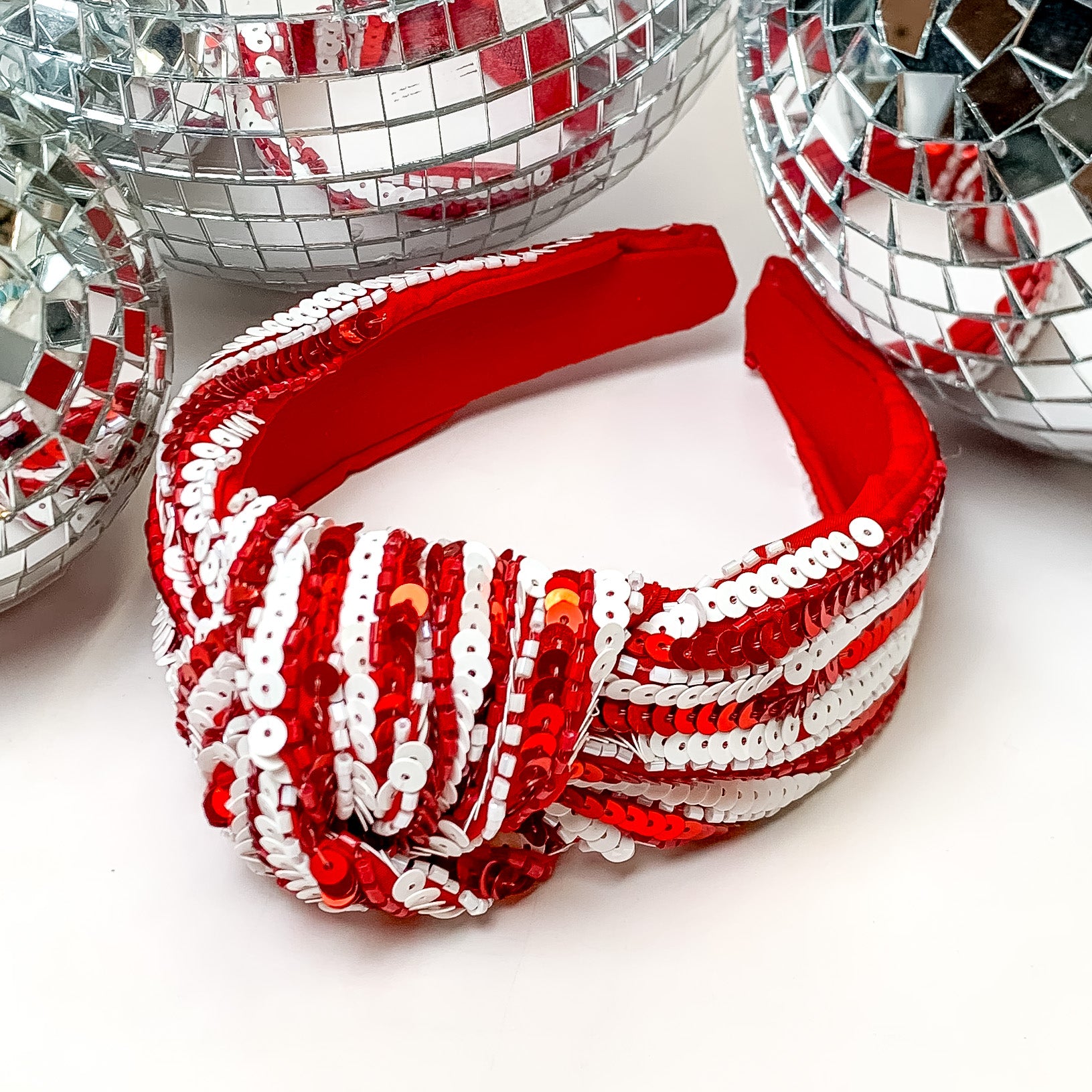 Striped Sequin Large Knot Headband in Red and White. This headband is pictured on a white background with disco balls behind the headband.
