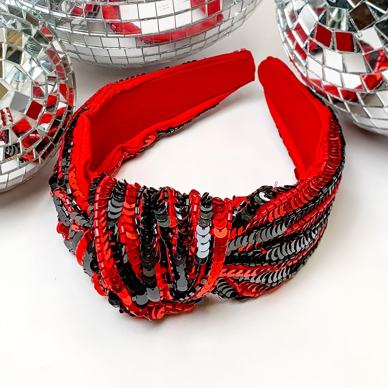 Striped Sequin Large Knot Headband in Red and Black. This headband is pictured on a white background with disco balls behind the headband.