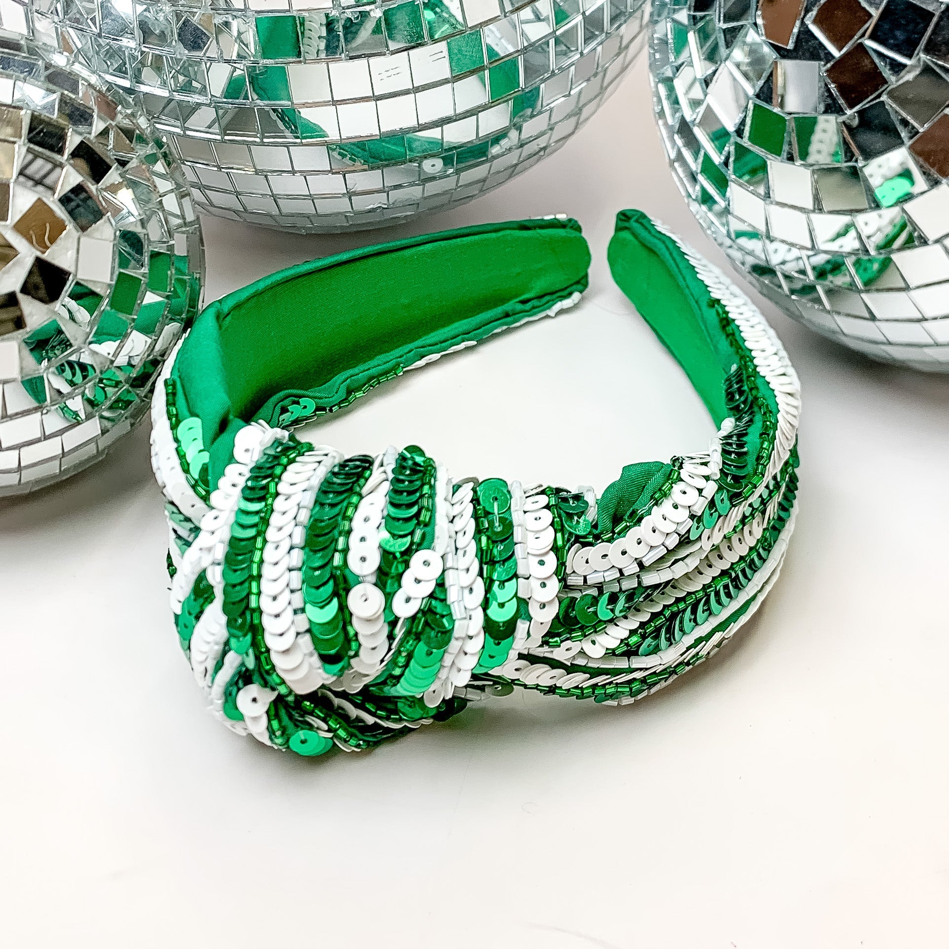 Striped Sequin Large Knot Headband in Green and White. This headband is pictured on a white background with disco balls behind the headband.