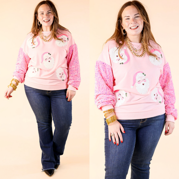 A woman wearing a light pink sequin Santa sweatshirt with velvet sleeves, paired with jeans and standing against a neutral background.