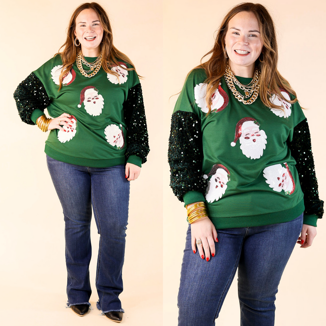 A woman wearing a dark green sweatshirt with sequin Santa icons and velvet sleeves, paired with jeans.