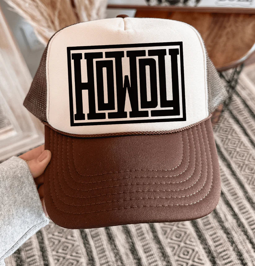 Brown and cream foam trucker hat with bold black serif “Howdy” graphic on front, mesh back, and snapback closure.