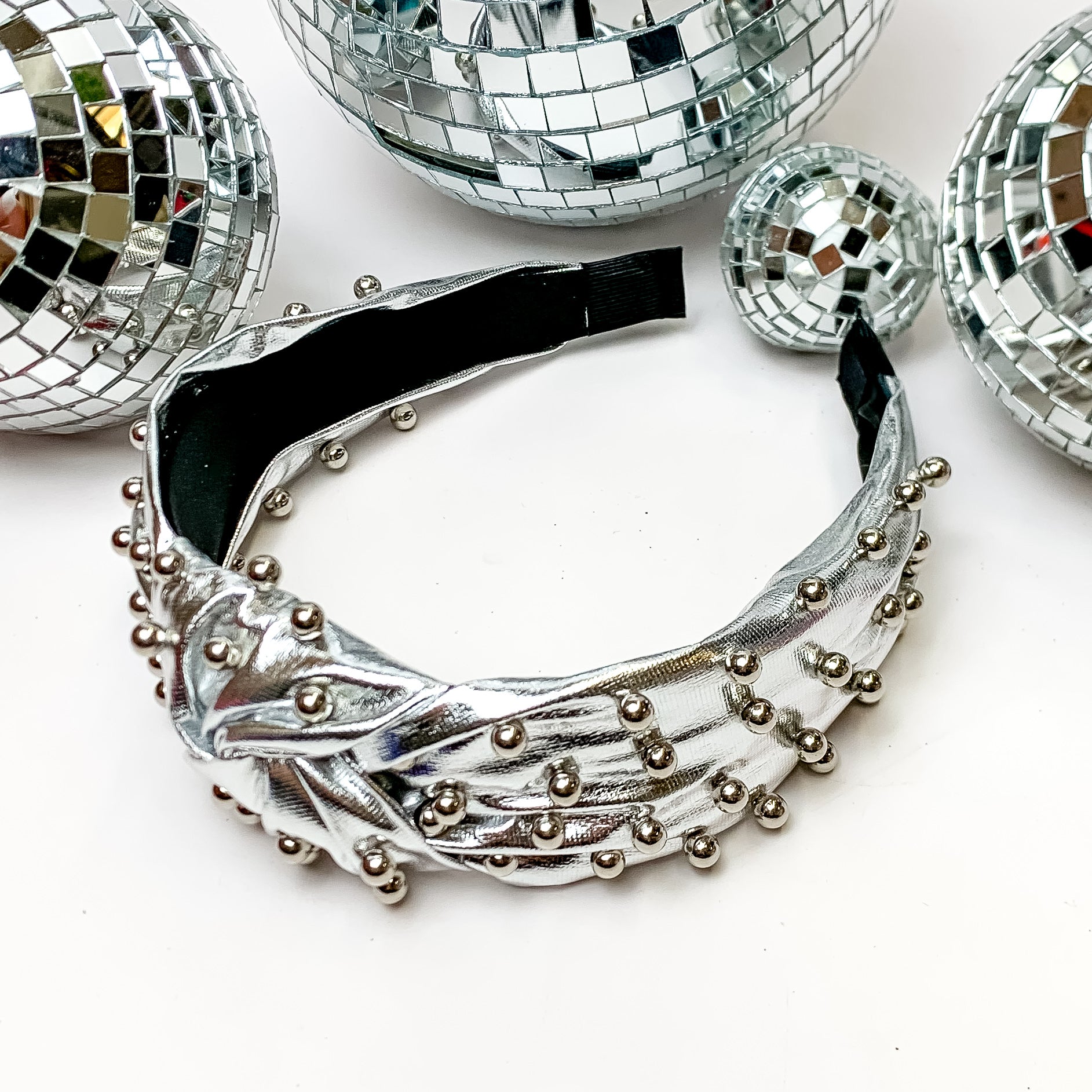 Top of the Charts Silver Headband With Silver Pearls. This headband is pictured on a white background and is surrounded by disco balls. 
